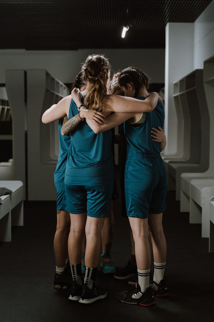 A women's basketball team shares a moment of unity huddling in a locker room.